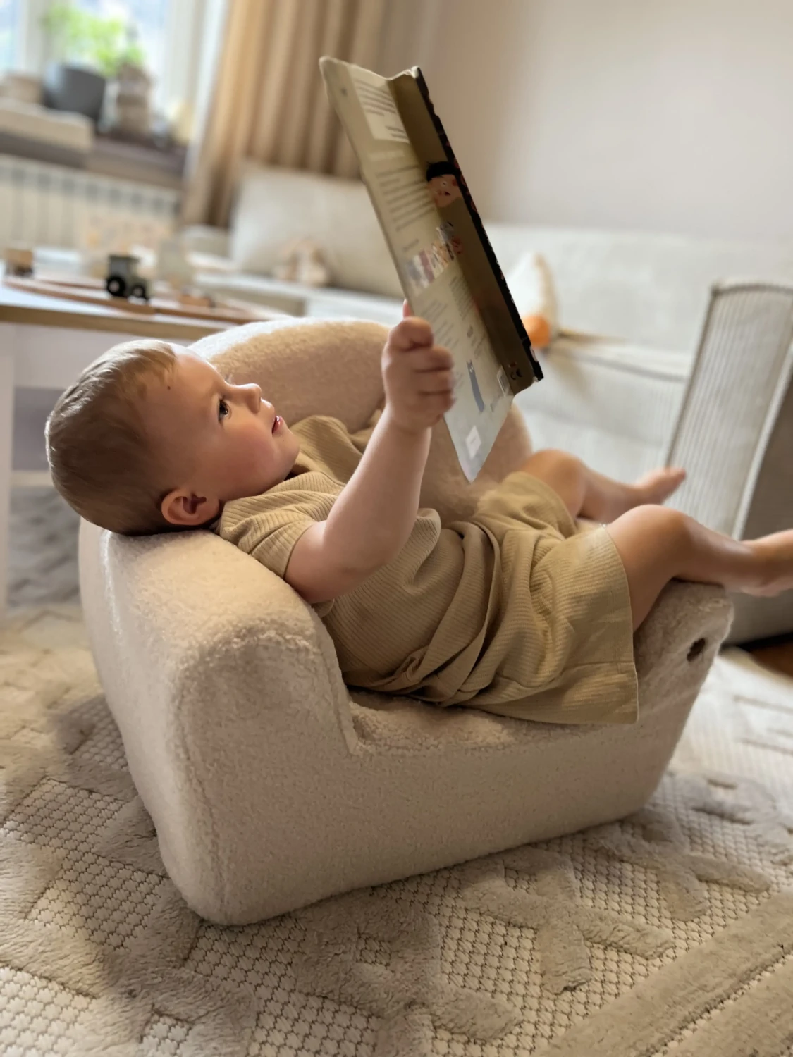 Ein Kind liest ein Büchlein und sitzt auf dem Schaumstoffsessel BUBU